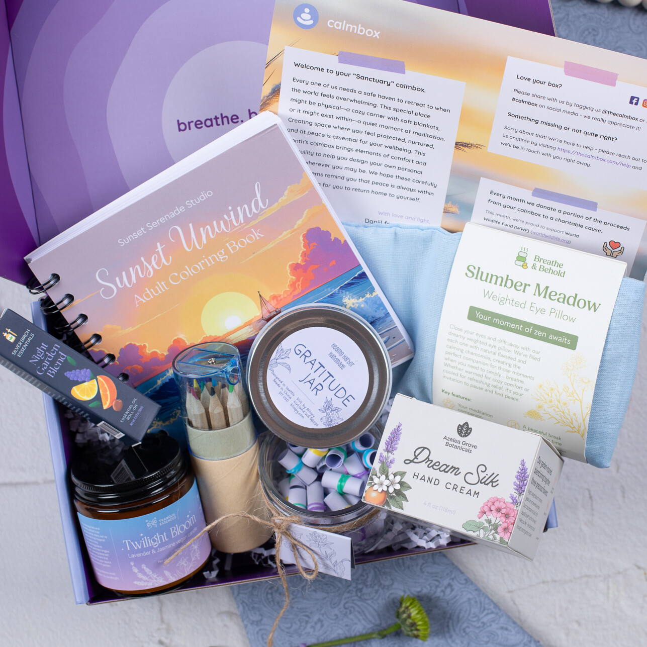 open calmbox with a sunset coloring book, pencils and crayons, a candle, hand cream and an eye pillow